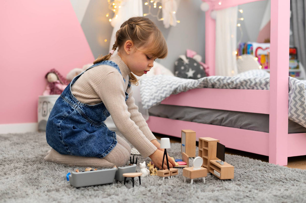 A young girl playing with a wooden miniature furniture set on the floor of her pink bedroom