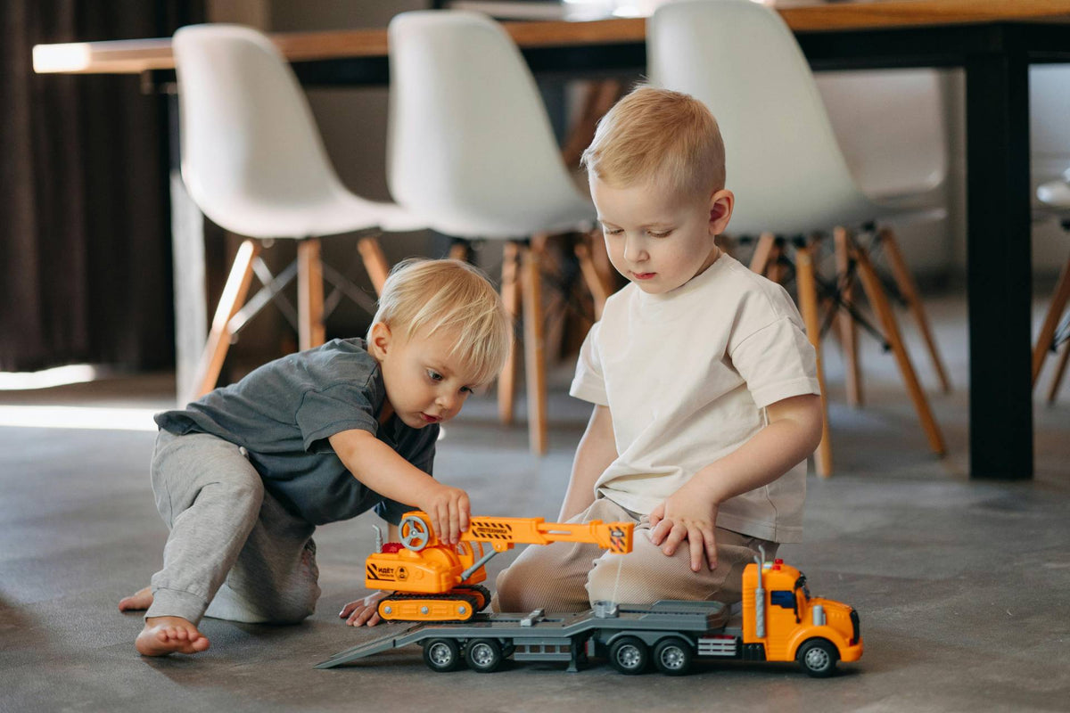 Two young children playing with toy construction trucks on the floor