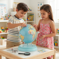 Boy in striped tee pinning red location marker on globe while girl in pink floral dress watches with compass magnifying glass and country fact cards on table