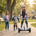 Girl in striped jacket and rainbow helmet riding Segway Electric Personal Transporter with biggest smile knee and elbow pads on two friends running alongside on golden hour autumn park path