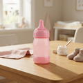 Pink baby feeding bottle on wooden nursery table with baby booties and cream