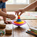 Parent and child spinning rainbow top together on wooden playroom floor with yo-yos and marbles nearby
