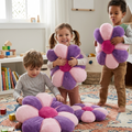 Three children in a bright playroom each hugging a large Daisy Flower Floor Cushion in pink and purple