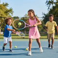 Three children laughing and playing tennis on a bright blue court with rainbow gradient junior rackets and yellow tennis balls