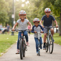 Three children confidently riding bikes and a scooter together through a sunny park path all wearing matching multi-sport helmets
